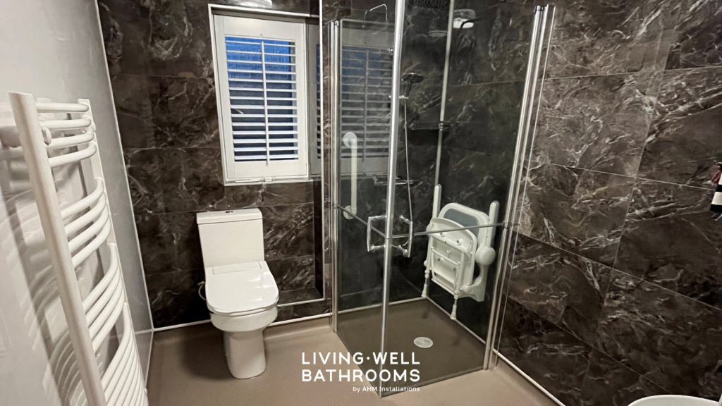 Wet room with screen enclosure, drop down shower seat white toilet and black marble panelled walls.